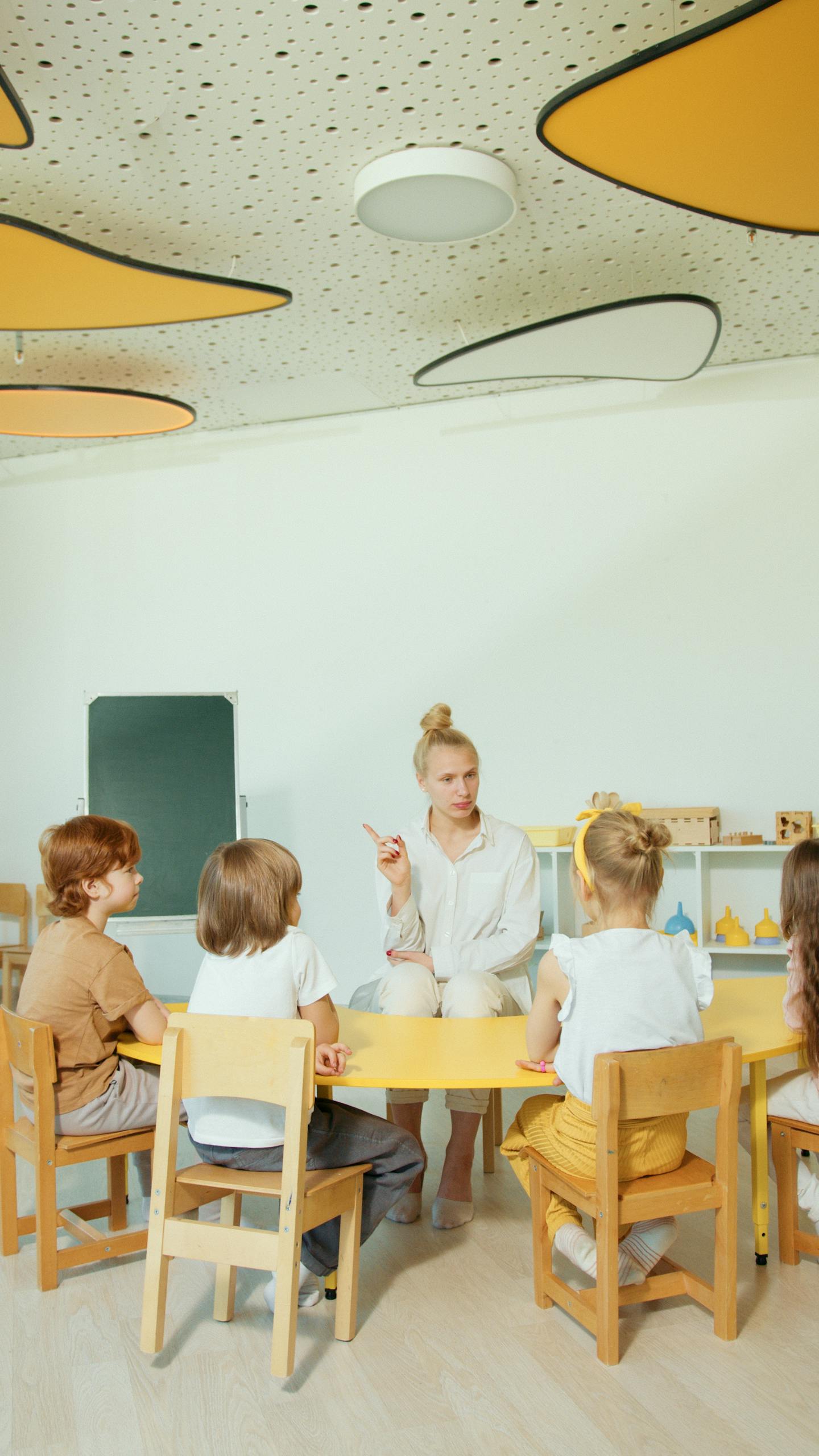 Children gathered around a teacher in a vibrant, modern classroom setting.