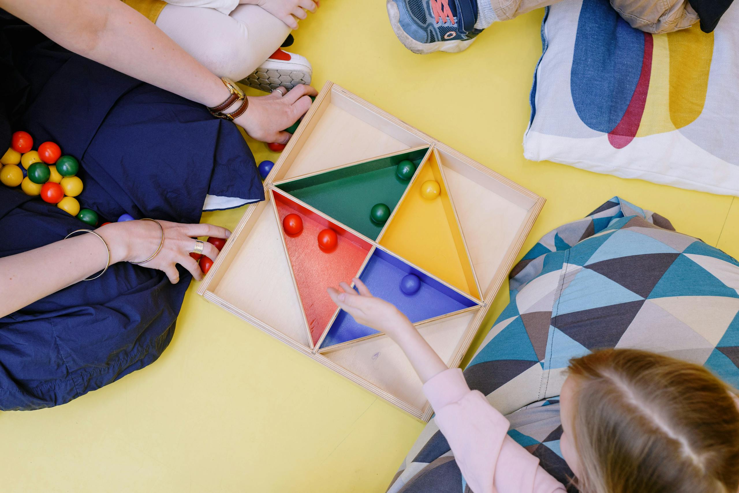 Children playing with a vibrant geometric puzzle on a yellow floor.