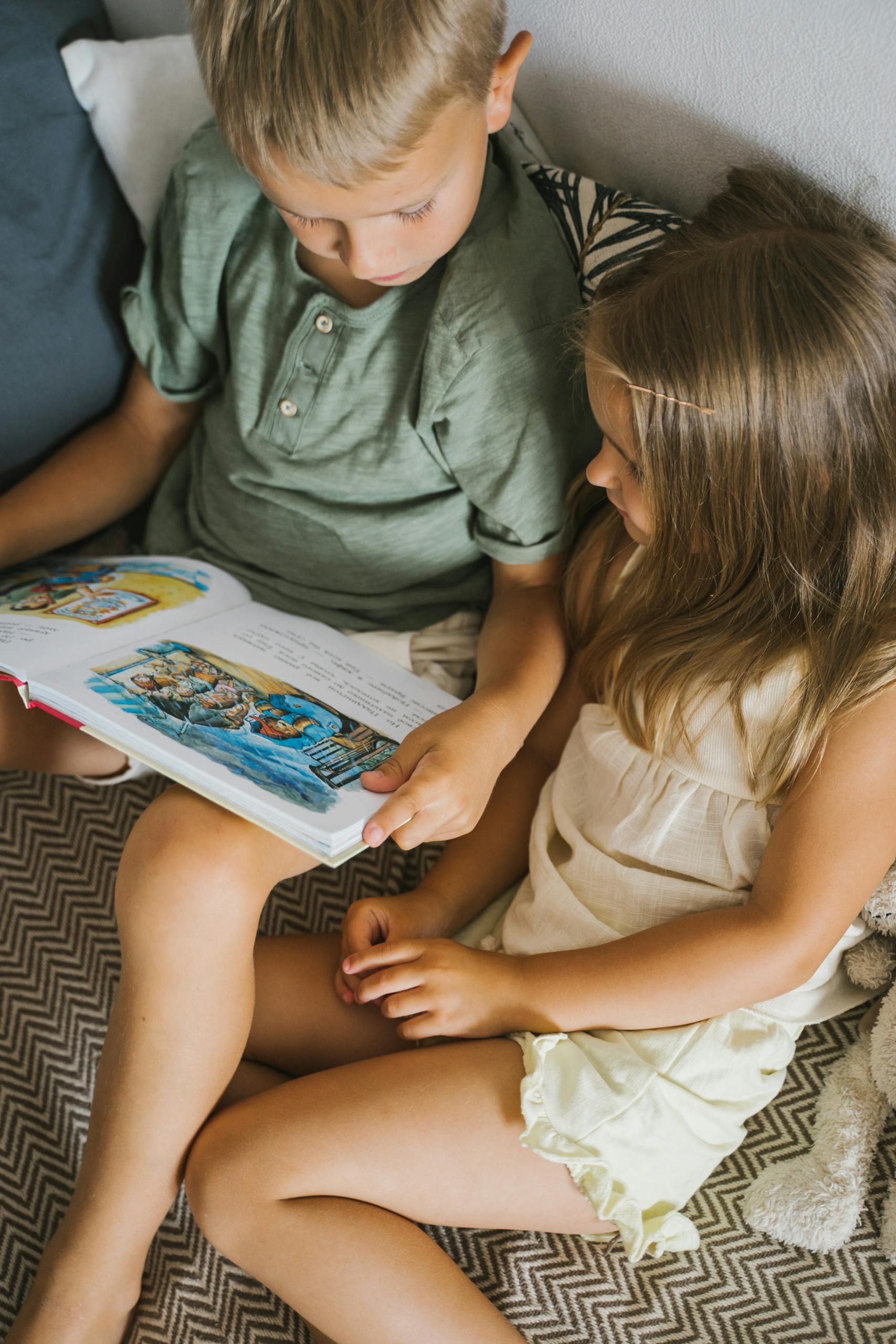 Two children reading a colorful storybook on a cozy bed indoors.