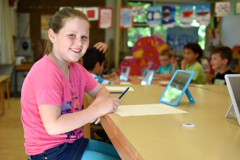 Smiling girl in a bright classroom during a lesson with classmates engaging in learning activities.