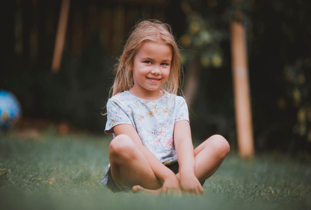 Young girl enjoys a sunny day sitting on grass, expressing joy and innocence.